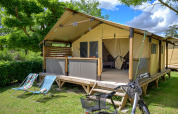 Safaritent Lodge Bali Confort 30m² op Camping Le Château in Frankrijk met ligstoelen en fiets buiten.
