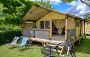 Tente safari Lodge Bali Confort 30m² au Camping Le Château en France, avec chaises longues et vélo devant.
