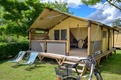 Safari-Zelt Lodge Bali Confort 30m² auf Camping Le Château in Frankreich mit Liegestühlen und Fahrrad davor.