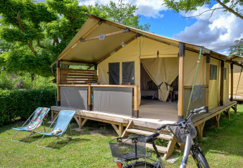 Tente safari Lodge Bali Confort 30m² au Camping Le Château en France, avec chaises longues et vélo devant.