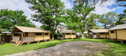Safaritenten Lodge Bali Confort op Camping Le Château in Frankrijk, omringd door gras en hoge bomen.