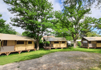 Safari tents Lodge Bali Confort at Camping Le Château in France, surrounded by green grass and tall trees.