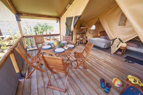 Tienda safari Lodge Bali Confort en Camping Le Château, Francia, con terraza de madera, mesa y camas.