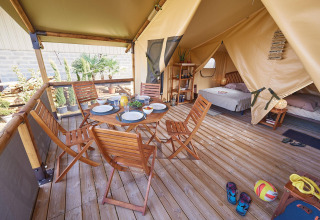 Safaritent Lodge Bali Confort op Camping Le Château in Frankrijk met houten terras, tafel en bedden.