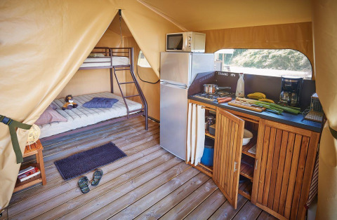 Binnenkant van Lodge Bali Confort 30m² safaritent bij Camping Le Château, met keuken en stapelbed.