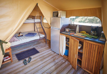 Inside a Lodge Bali Confort 30m² safari tent at Camping Le Château, featuring a kitchen and bunk bed.