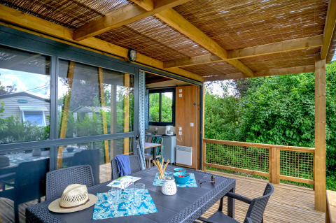 Træterrasse med spisebord og stole på Cottage Morea, omgivet af frodig natur og moderne indretning.