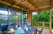 Covered wooden terrace with dining table at Cottage Morea, surrounded by lush greenery and modern comforts.