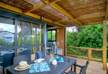 Covered wooden terrace with dining table at Cottage Morea, surrounded by lush greenery and modern comforts.