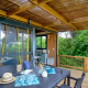 Terrasse en bois couverte avec table à manger au Cottage Morea, entourée de verdure et d’une ambiance moderne.