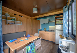 Moderne Küche und Essbereich im Cottage Morea, Camping Le Château, Frankreich, mit Holzmöbeln und Fenstern.