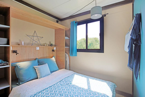 Camera da letto moderna e luminosa al Cottage Morea nel Camping Le Château, Francia, con letto matrimoniale.