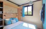 Modern en licht slaapkamerinterieur in Cottage Morea op Camping Le Château, Frankrijk, met tweepersoonsbed.