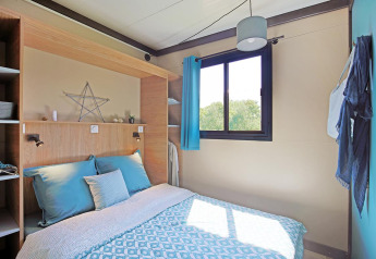 Modernes Schlafzimmer im Cottage Morea im Camping Le Château, Frankreich, mit Tageslicht und bequemer Bettwäsche.