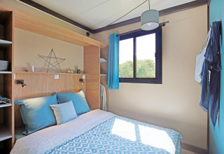 Camera da letto moderna e luminosa al Cottage Morea nel Camping Le Château, Francia, con letto matrimoniale.