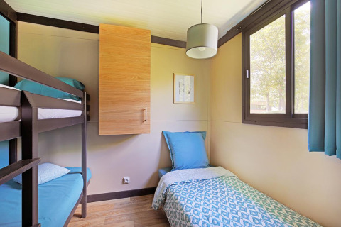 Lichte kamer met stapelbed en eenpersoonsbed in Cottage Morea, Camping Le Château, Frankrijk, raamzicht.