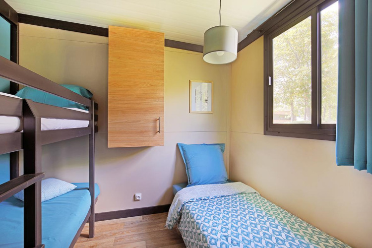 Lyst værelse med køjesenge og enkeltseng på Cottage Morea, Camping Le Château, Frankrig, med vindue.