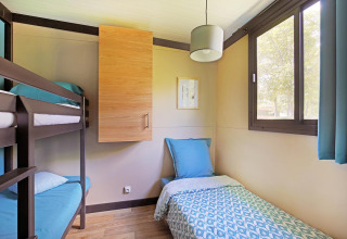 Camera luminosa con letto a castello e singolo in Cottage Morea, Camping Le Château, Francia, ampia finestra.