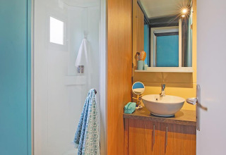 Moderne badeværelse i Cottage Morea på Camping Le Château, med træskabe, bruser og spejl.