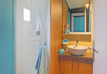 Modernes Badezimmer im Cottage Morea im Camping Le Château, mit Dusche, Holzschränken und Waschbecken.