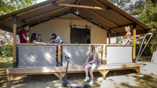 Famiglia si gode il tempo all'aperto davanti a una tenda safari Lodge Kenya con monopattino elettrico.