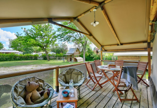 Acogedora terraza en la tienda safari Lodge Kenya en Camping Le Château, Francia, con asientos y vistas verdes.