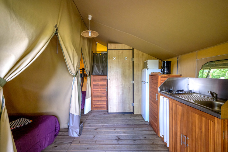 Interior view of the Lodge Kenya safari tent at Camping Le Château in France, featuring a kitchen and bed.
