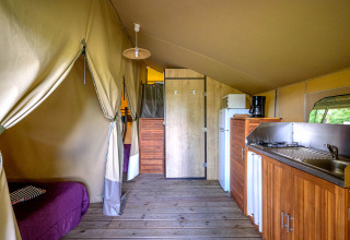 Vista interior de la tienda safari Lodge Kenya en Camping Le Château, Francia, con cocina y cama visible.