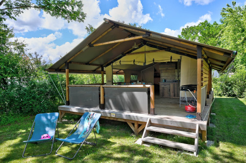 Safari-Zelt Lodge Kenya Vintage mit Terrasse, Liegestühlen und Grill, umgeben von viel Grün an einem klaren Tag.