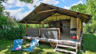 Tienda de safari Lodge Kenya Vintage con terraza abierta, sillas azules y vegetación alrededor en día soleado.