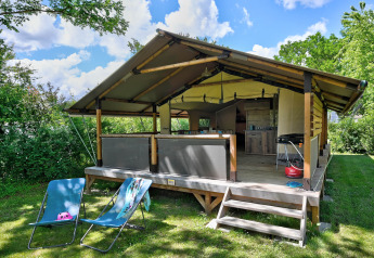 Safari-Zelt Lodge Kenya Vintage mit Terrasse, Liegestühlen und Grill, umgeben von viel Grün an einem klaren Tag.