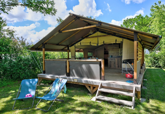 Safari-Zelt Lodge Kenya Vintage mit Terrasse, Liegestühlen und Grill, umgeben von viel Grün an einem klaren Tag.