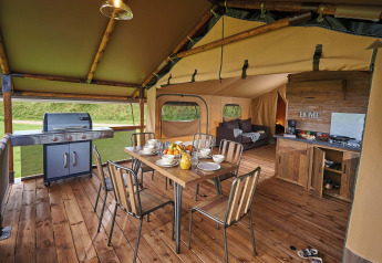 Interior of a safari tent Lodge Kenya Vintage at Camping Le Château, France, showing dining, grill and kitchen.