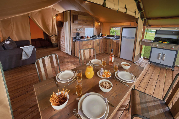 Interior of Lodge Kenya Vintage safari tent with modern kitchen and dining table at Camping Le Château, France.