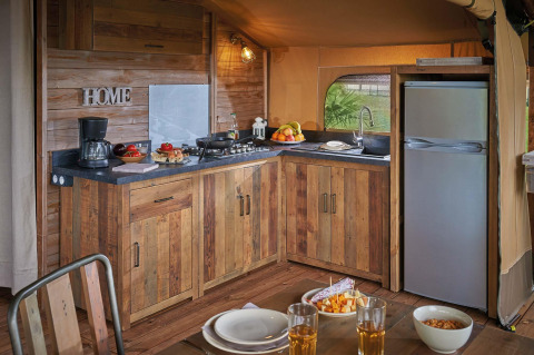 Kitchen in Lodge Kenya Vintage safari tent at Camping Le Château, France, with rustic wood cabinets and table.