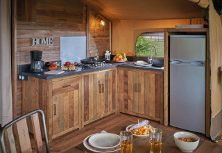 Kitchen in Lodge Kenya Vintage safari tent at Camping Le Château, France, with rustic wood cabinets and table.