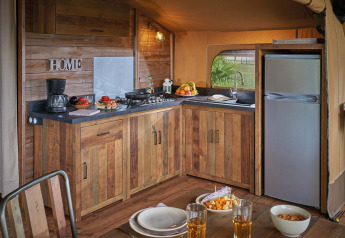 Küche im Lodge Kenya Vintage Safarizelt auf Camping Le Château, Frankreich, mit Holzmöbeln und Esstisch.