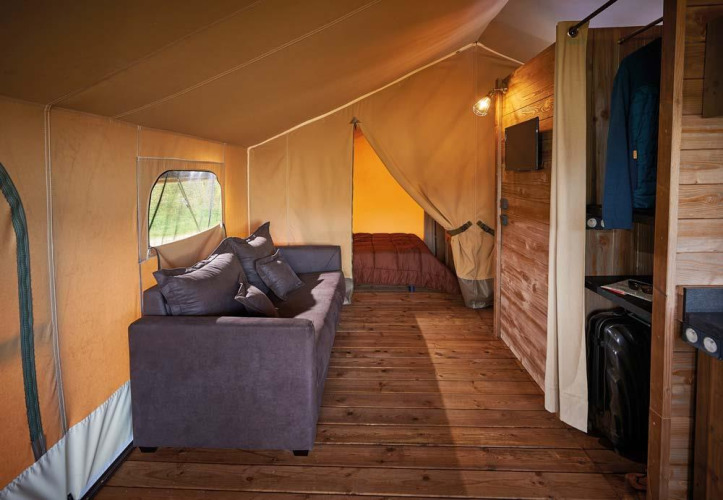 Binnenzijde van Lodge Kenya Vintage safaritent op Camping Le Château, Frankrijk, met sofa en bed.