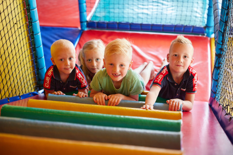 Cuatro niños juegan juntos en una colorida zona de juegos interior en un alojamiento glamping.