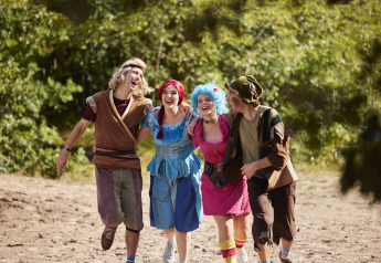 Four people in colorful costumes smiling and walking arm in arm outdoors at a glamping accommodation.