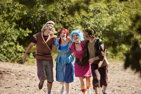 Quattro persone in costume colorato ridono insieme all’aperto in una struttura di glamping immersa nel verde.