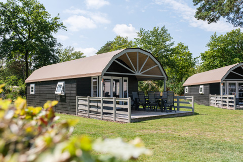 Außenaufnahme einer Vechtdallodge im Kampeerdorp de Zandstuve in den Niederlanden mit Terrasse und Sitzgruppe.