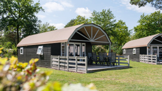 Buitenaanzicht van een Vechtdallodge bij Kampeerdorp de Zandstuve in Nederland met terras en tuinstoelen.
