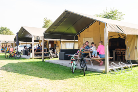Familia disfruta frente a una tienda safari en Kampeerdorp de Zandstuve, Países Bajos, con bicicletas y bancos.