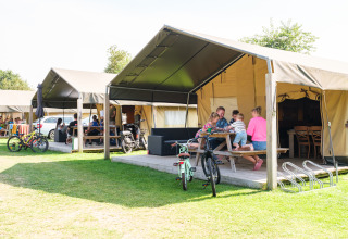 Familia disfruta frente a una tienda safari en Kampeerdorp de Zandstuve, Países Bajos, con bicicletas y bancos.