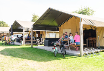 Familie genießt Zeit vor einem Safarizelt im Kampeerdorp de Zandstuve, Niederlande, mit Fahrrädern und Tischen.