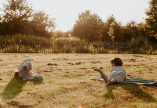 Twee kinderen spelen op het gras bij zonsondergang in vakantiepark REBL Outdoor in Friesland, Nederland.