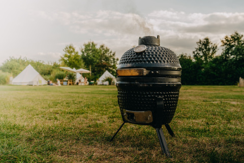 Zwarte keramische barbecue op de weide, glampingtenten en mensen op de achtergrond bij REBL Outdoor, Friesland.