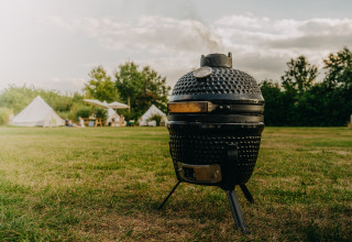 Zwarte keramische barbecue op de weide, glampingtenten en mensen op de achtergrond bij REBL Outdoor, Friesland.