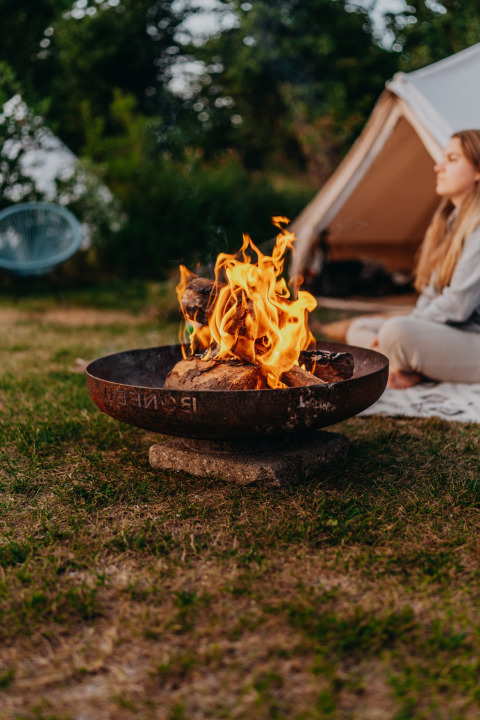 Falò davanti a una tenda al parco vacanze REBL Outdoor in Frisia, Paesi Bassi, con una persona seduta.